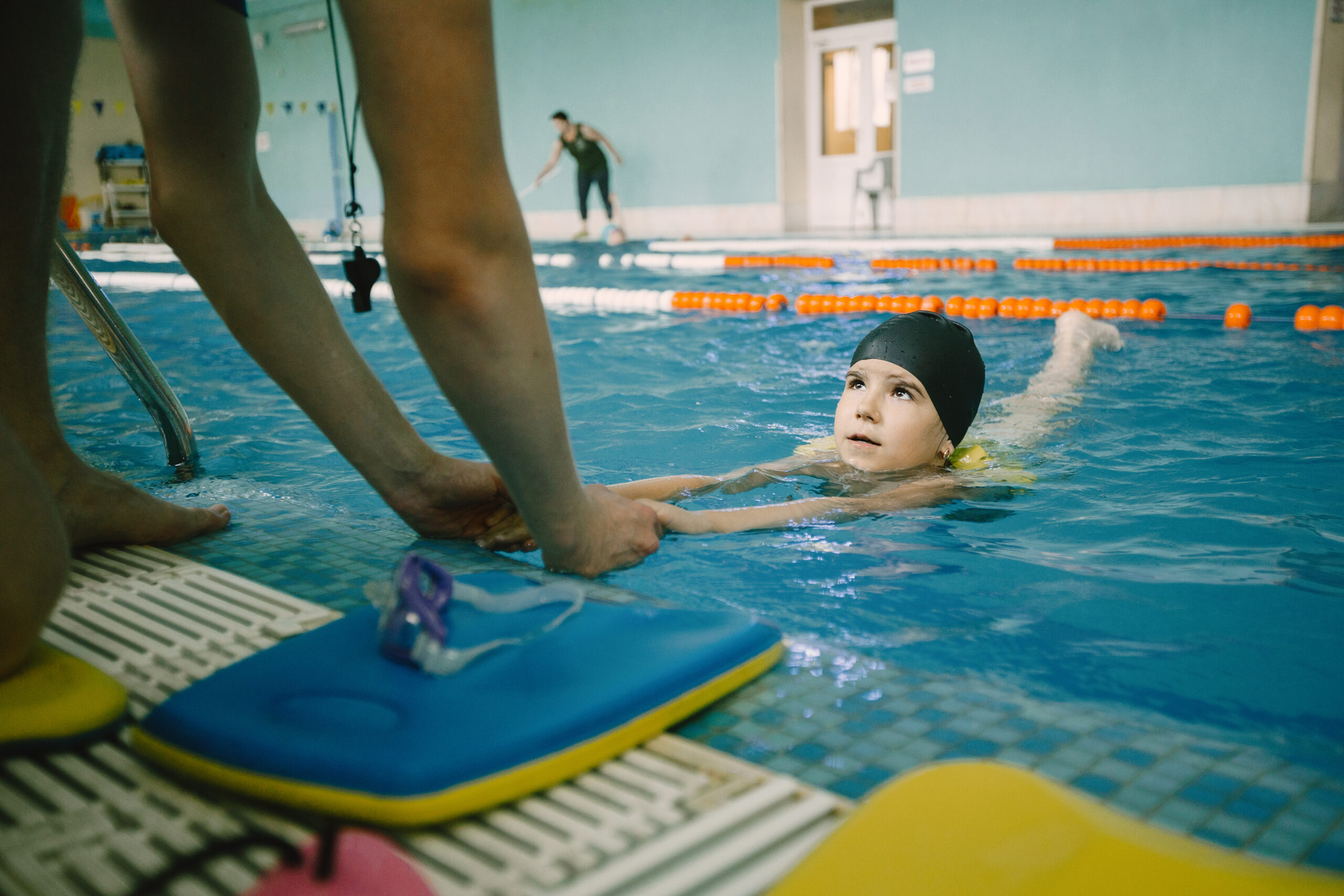 Coach teaching kid in indoor swimming pool how to swim and dive. Swimming lesson, kids development.