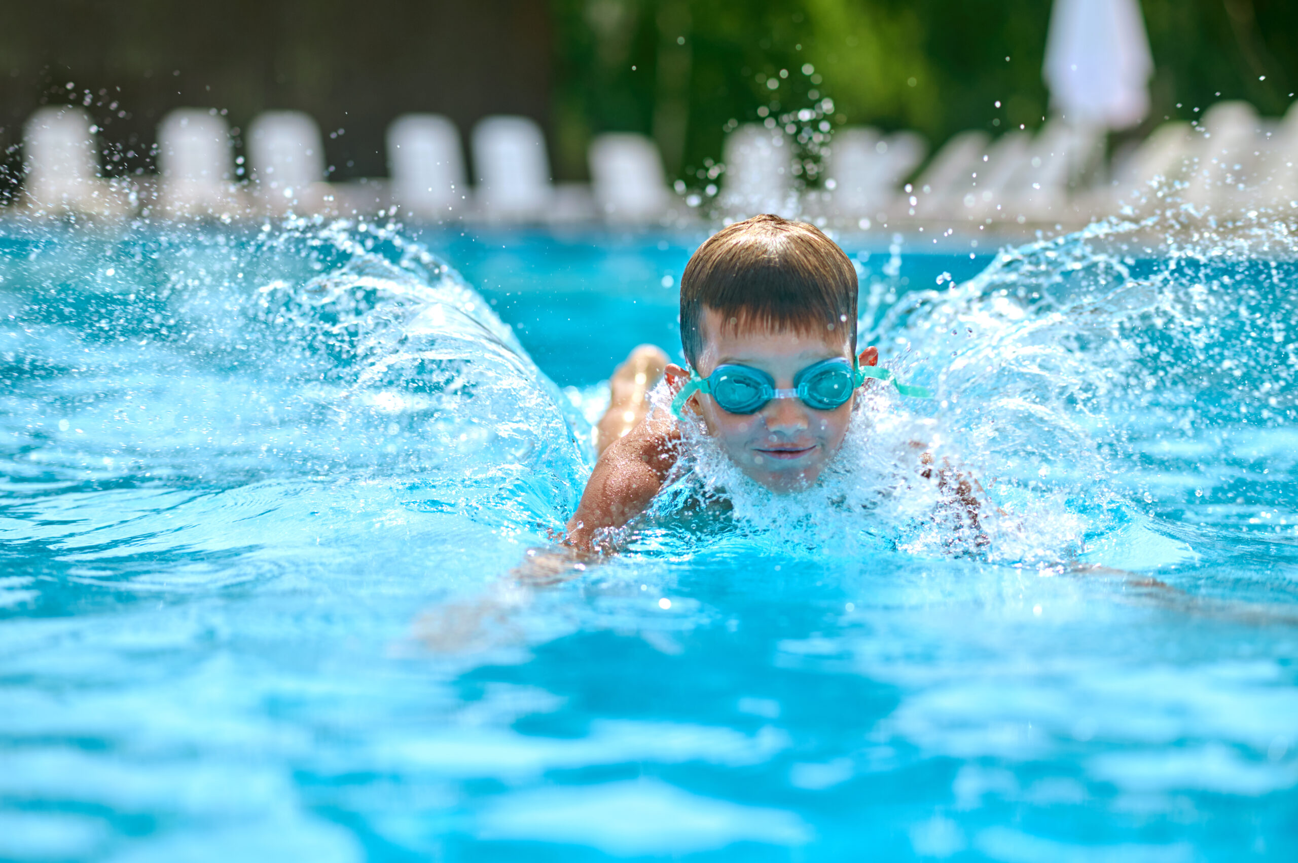 Pleasure, swimming. Boy in swimming goggles vigorously swimming splashing in pool outdoors on fine day